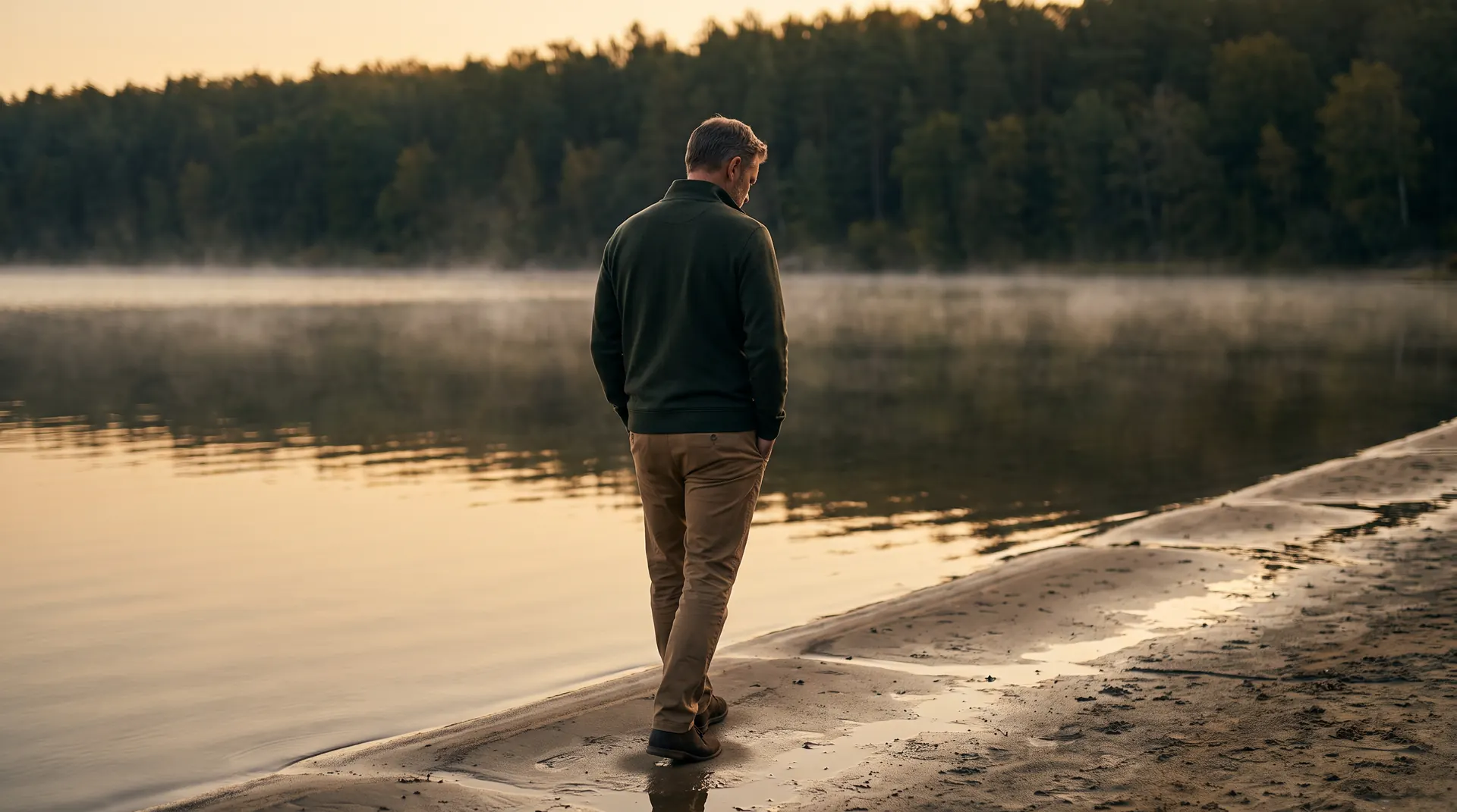 A leader walking alone along a still lakeshore at dawn