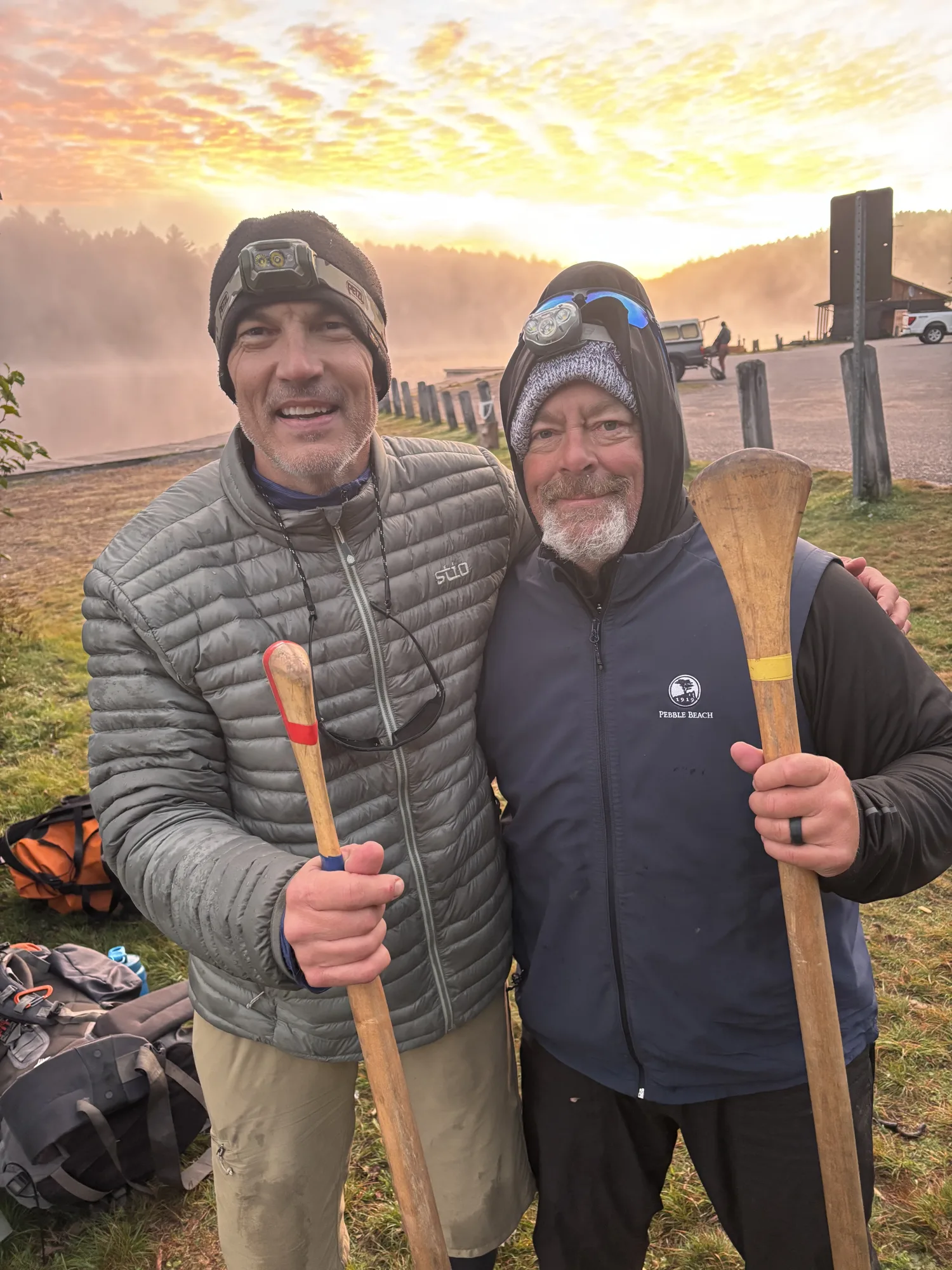 Dr. Chad Norris and a fellow expedition member holding canoe paddles on a misty Canadian lakeshore at sunrise