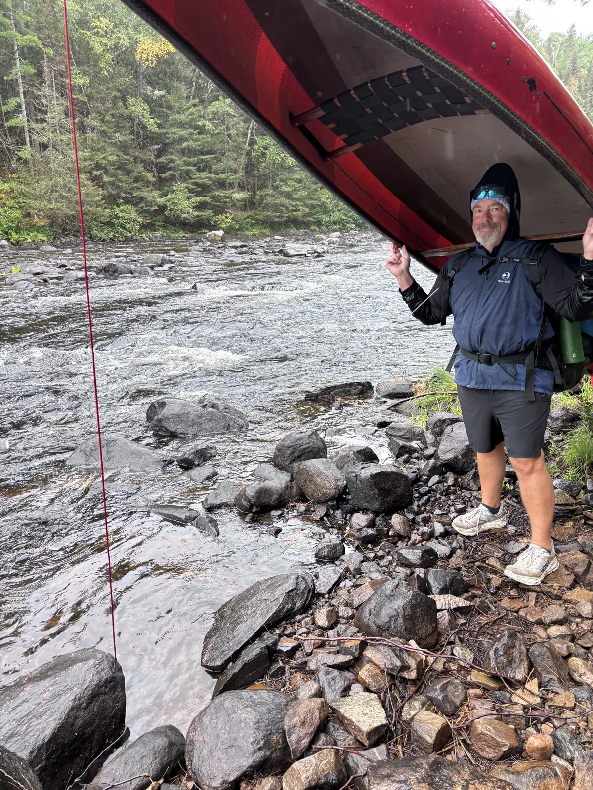 Dr. Chad Norris carrying a canoe overhead along a rocky river portage in the Canadian wilderness